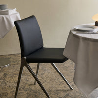 Black minimalist chair with sleek silver legs, set against a neutral background and textured flooring.