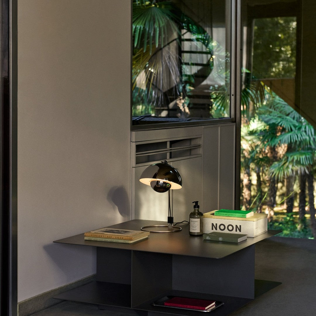 Modern black table with sleek design, accented by a white lamp and green book, surrounded by lush greenery.