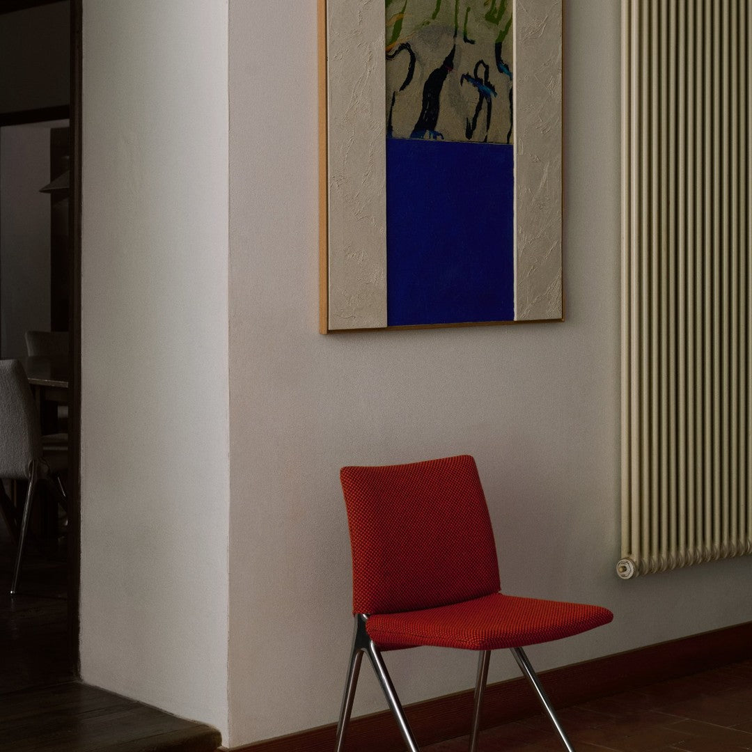 Vibrant red chair against a minimalist wall with abstract blue and green artwork, creating a modern aesthetic.