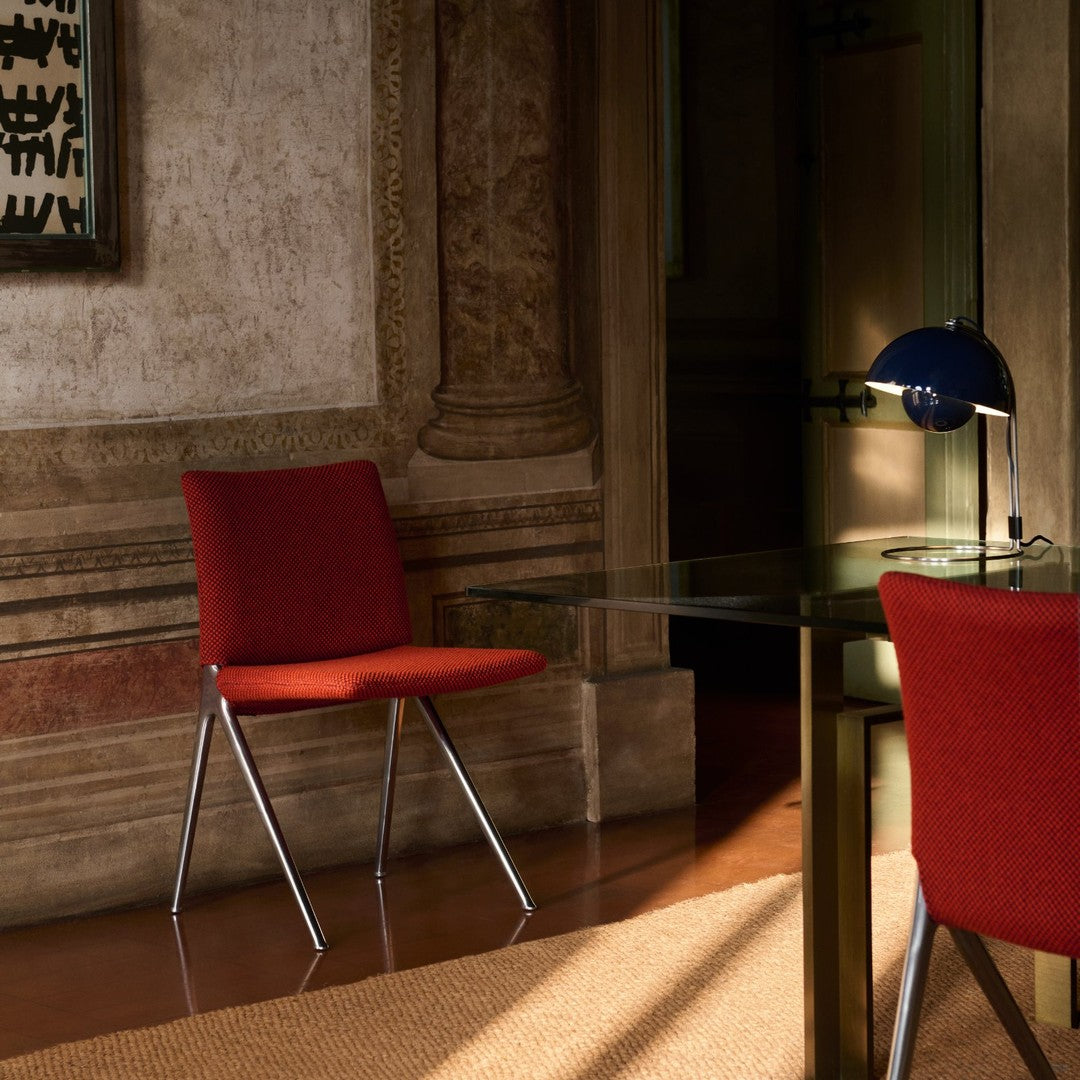 Red upholstered chair with sleek metal legs, placed beside a glass table and set against a warm-toned room.