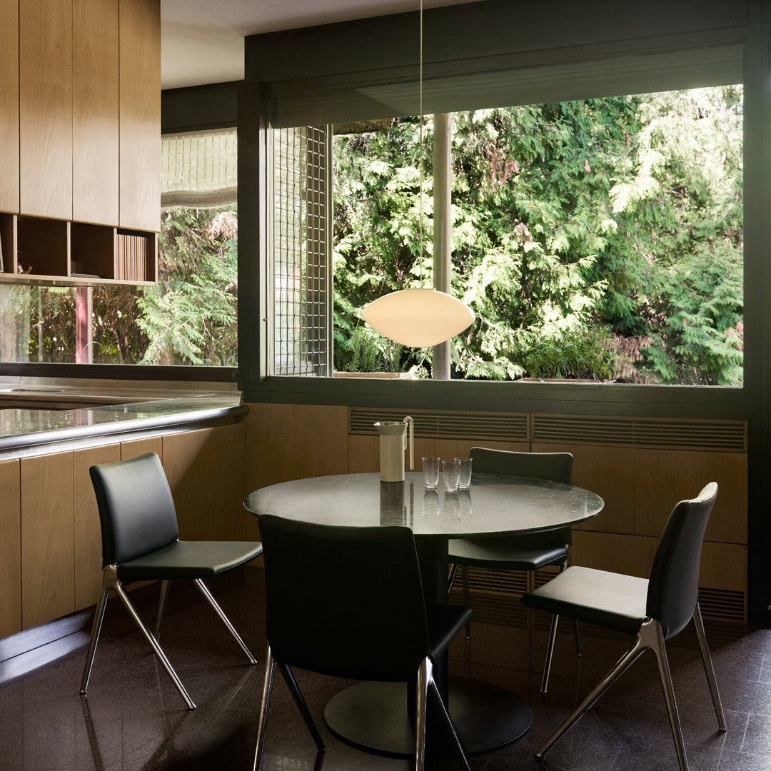 Modern kitchen featuring a sleek black table, black chairs, and warm wood cabinetry against a vibrant green garden view.