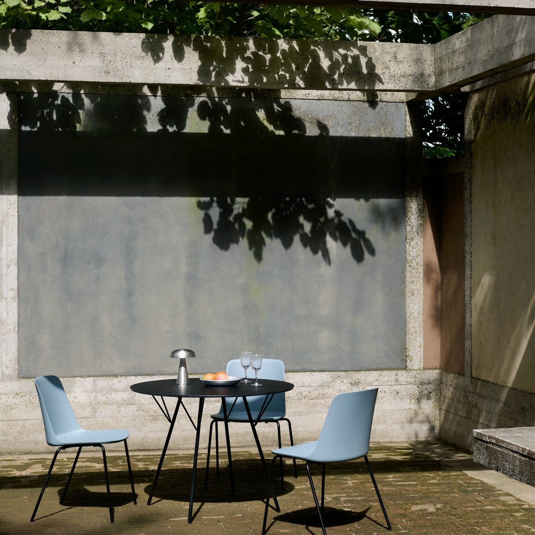 Light blue chairs and a black round table set against a textured concrete backdrop in a serene outdoor setting.
