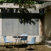 Light blue chairs and a black round table set against a textured concrete backdrop in a serene outdoor setting.