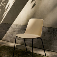 Beige minimalist chair with smooth surface and black metal legs, set against a textured concrete backdrop with soft shadows.