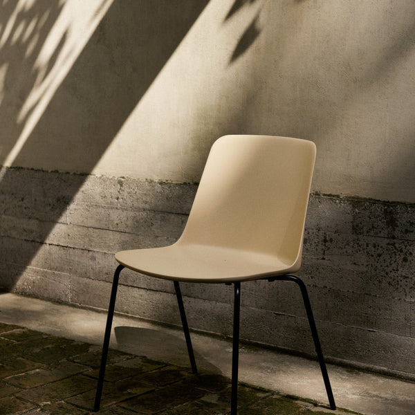 Beige minimalist chair with smooth surface and black metal legs, set against a textured concrete backdrop with soft shadows.