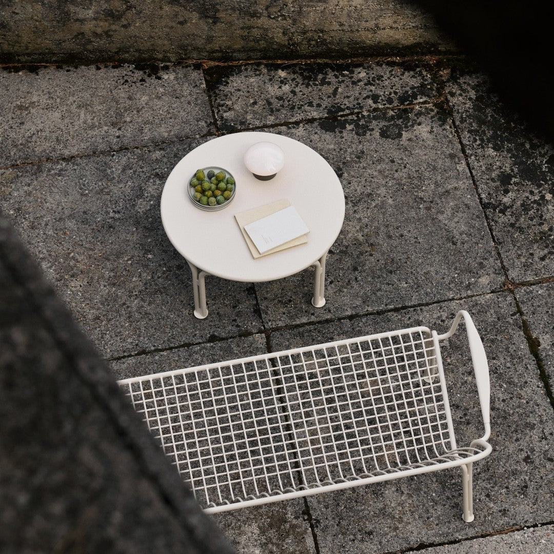 White round table with green bowl and patterned woven bench on a textured grey surface.