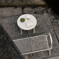 White round table with green bowl and patterned woven bench on a textured grey surface.