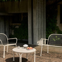 Modern white outdoor chairs and round table on textured stone patio, surrounded by lush green foliage.