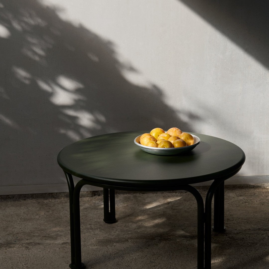 Round green table with a glossy finish and black legs, featuring a bowl of bright yellow oranges.
