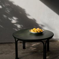 Round green table with a glossy finish and black legs, featuring a bowl of bright yellow oranges.