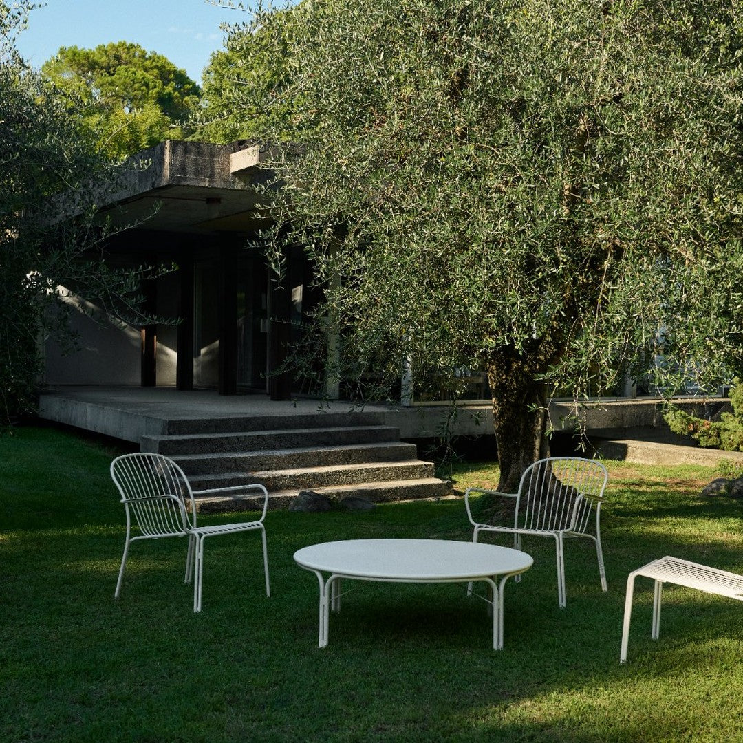 White outdoor furniture set featuring sleek lines, paired with a lush green garden backdrop.