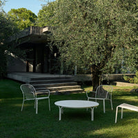 White outdoor furniture set featuring sleek lines, paired with a lush green garden backdrop.