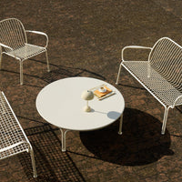 White metal patio chairs and round table with a minimalist design and a textured dark ground.