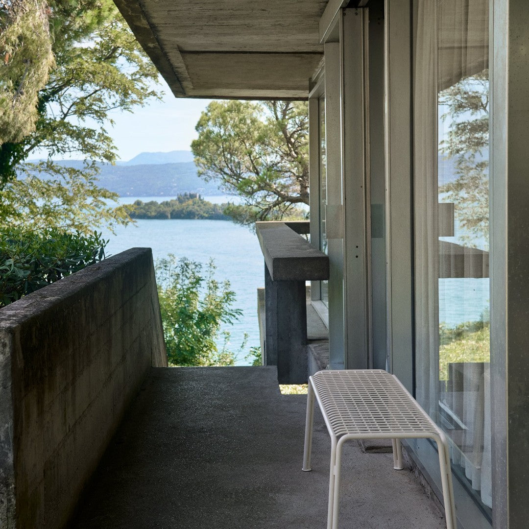 Minimalist white bench on a concrete porch with a view of green trees and blue water, highlighting modern outdoor aesthetics.
