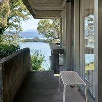 Minimalist white bench on a concrete porch with a view of green trees and blue water, highlighting modern outdoor aesthetics.