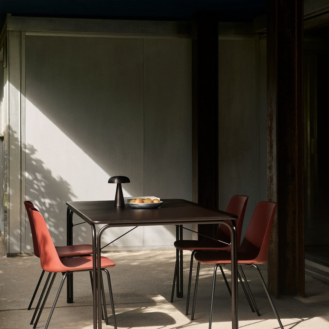 Modern black table and four burgundy chairs, with a minimalist design and natural light creating soft shadows.