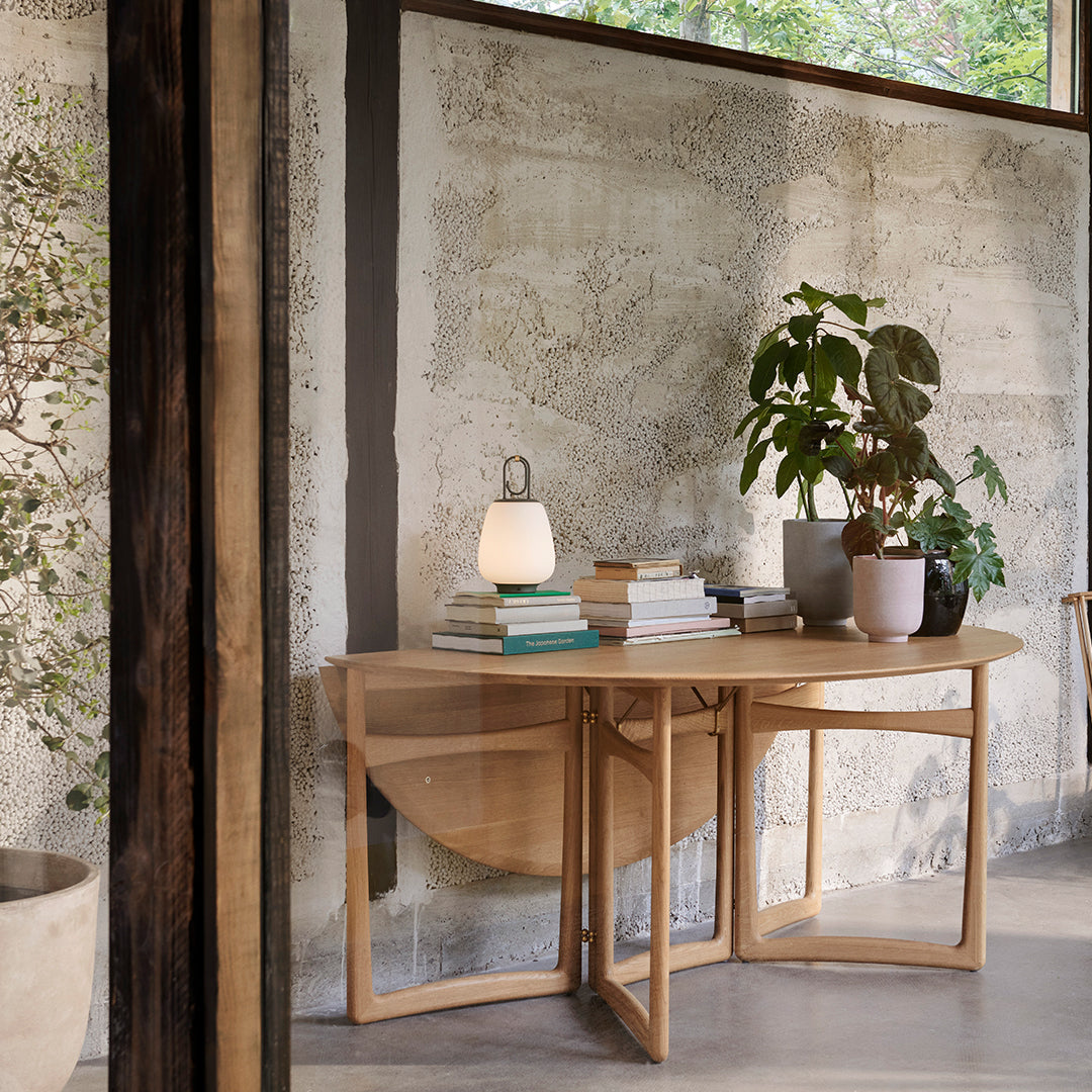Wooden console table with a light natural finish, complemented by greenery and soft white accents.