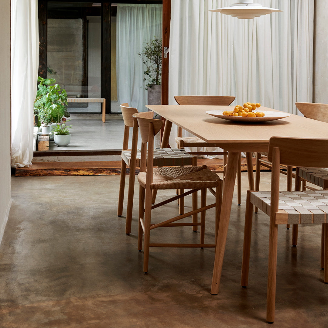 Light wooden dining table with natural grain, paired with beige upholstered chairs, set in a minimalistic, earthy-toned room.