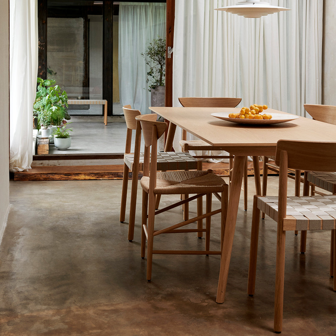 Light wood dining table with natural textures, woven chair patterns, and neutral tones in a minimalist space.