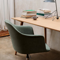 Green upholstered chair beside a wooden desk, with neutral decor and stacks of books, creating a serene workspace.