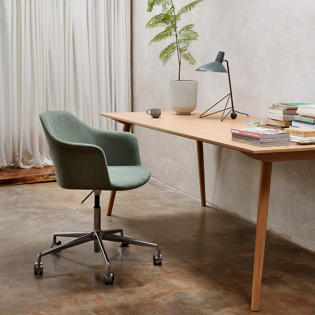 "Soft green upholstered chair with a sleek metallic base, set against a natural wood desk and neutral decor."