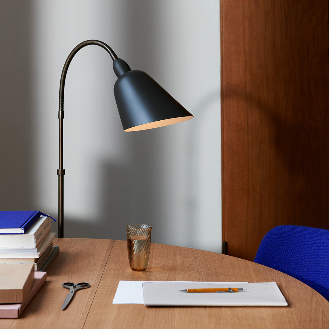 Black modern lamp with a warm gold interior, blue chair, wooden table, and stacked books in neutral tones.