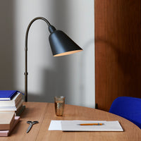 Black modern lamp with a warm gold interior, blue chair, wooden table, and stacked books in neutral tones.