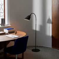 Black floor lamp casting a shadow in a minimalist space with a wooden table and deep blue chair.