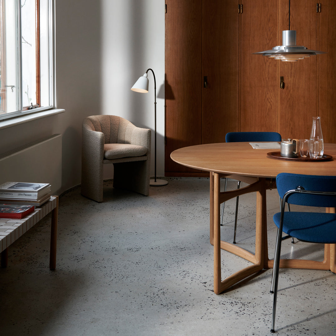 Modern dining room with a round wooden table, blue chairs, and beige accents in a minimalist, warm color palette.