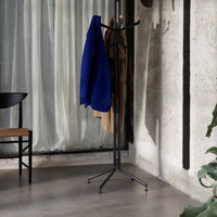 Black standing coat rack with blue and brown garments in a modern, minimalistic room setting.