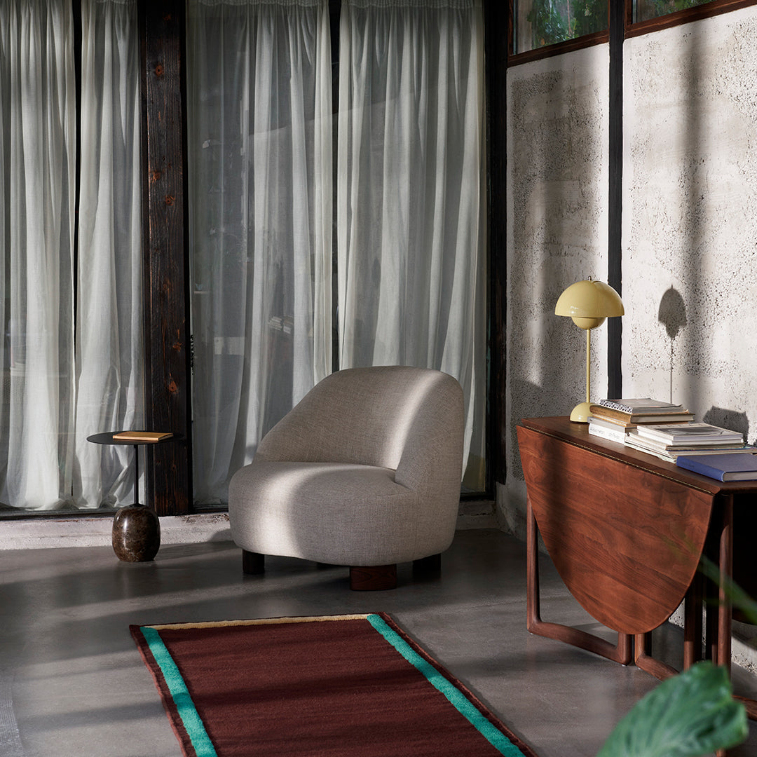 Soft cream armchair paired with a rich burgundy rug accented in teal, set against neutral-toned curtains and walls.