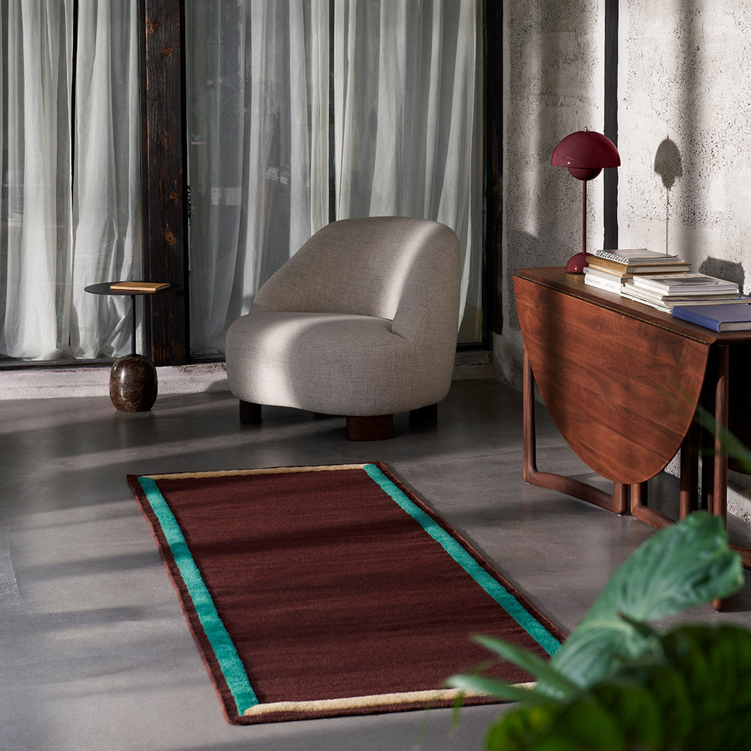 Rustic maroon rug with teal border complements modern interior decor. Elegant, bold design enhances any space.