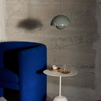 Modern blue accent chair with a minimalist white side table and a soft gray pendant light against textured gray wall.