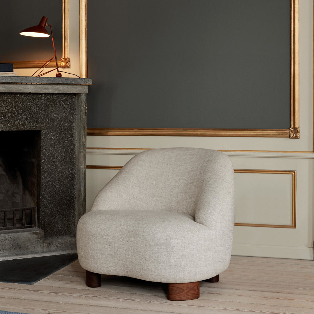 Curved beige chair with a textured fabric and wooden legs, set against a gray wall with gold accents.