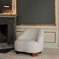 Curved beige chair with a textured fabric and wooden legs, set against a gray wall with gold accents.