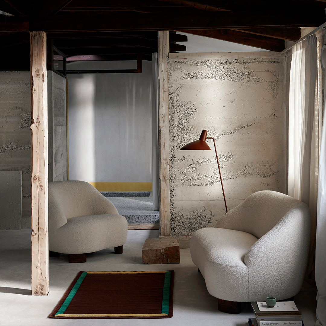 Cream and beige upholstered chairs with a marbled wall, accented by a red and green bordered rug. Modern interior design.