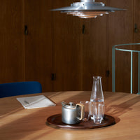 Silver teapot and glass carafe on a brown wooden tray, set against a warm, minimalist background.