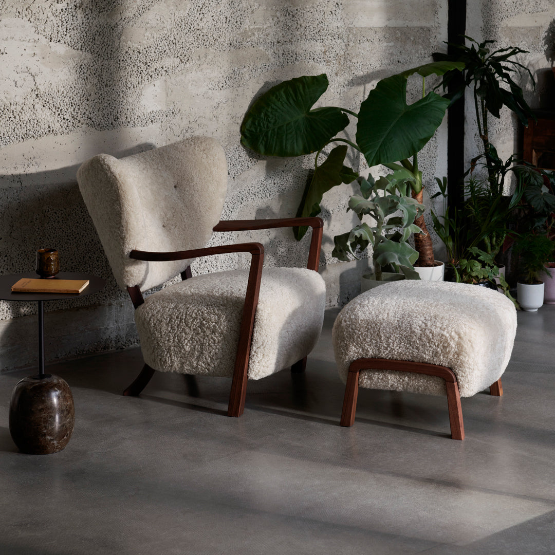 Cozy cream armchair and ottoman with a textured, plush finish, framed by dark wood accents and indoor greenery.