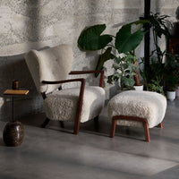 Cozy cream armchair and ottoman with a textured, plush finish, framed by dark wood accents and indoor greenery.