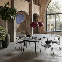 Modern dining room with a sleek black table, dark chairs, and burgundy pendant lights against a neutral backdrop.