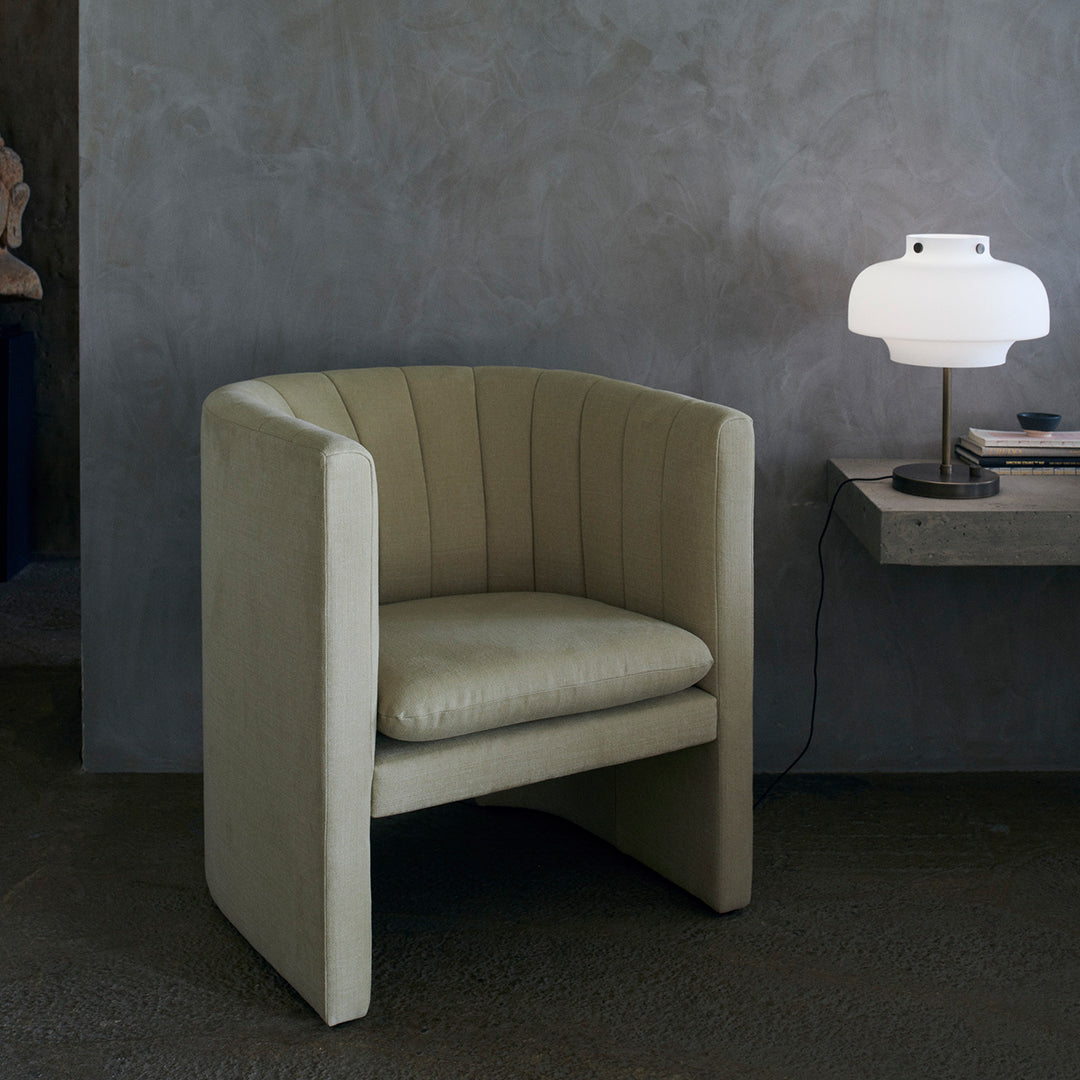 Modern olive green barrel chair with vertical stitching against a muted gray background. Ideal for contemporary decor.