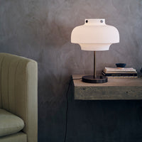 Modern white lamp with a matte finish, paired with dark wood and a grey-toned wall, enhancing minimalist aesthetics.