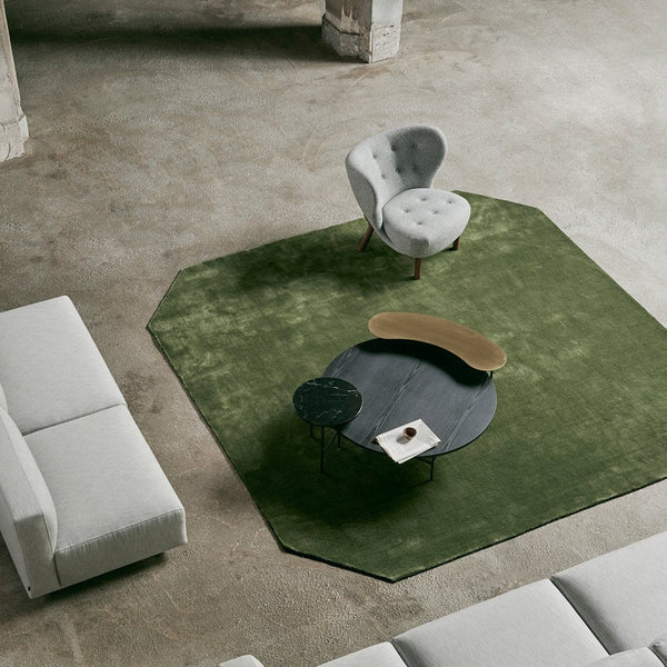 Green octagonal rug, gray tufted chair, round black table, minimalist decor. Modern, neutral color palette.