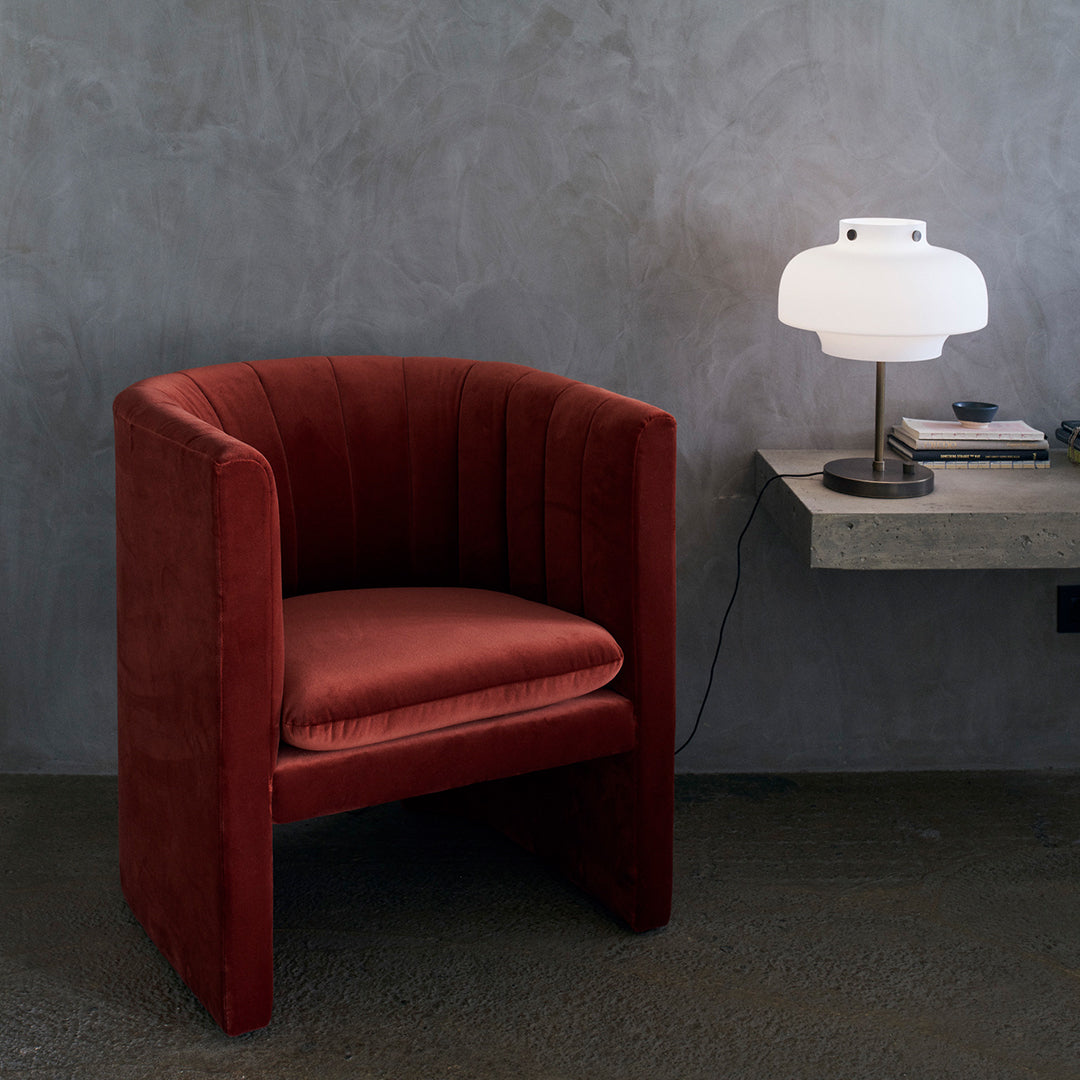 "Deep red upholstered armchair with vertical ribbed pattern against a minimalist gray backdrop."