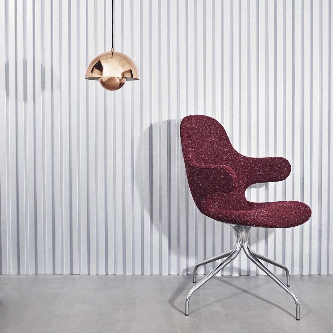 Burgundy upholstered chair with smooth, curvy design against a striped white wall and metallic pendant light.