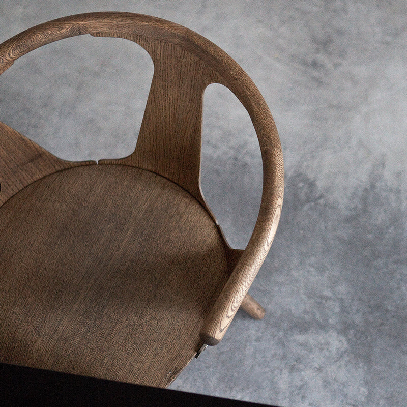 Wooden chair with a natural finish, featuring a smooth, minimalist design and subtle grain patterns against a light gray background.