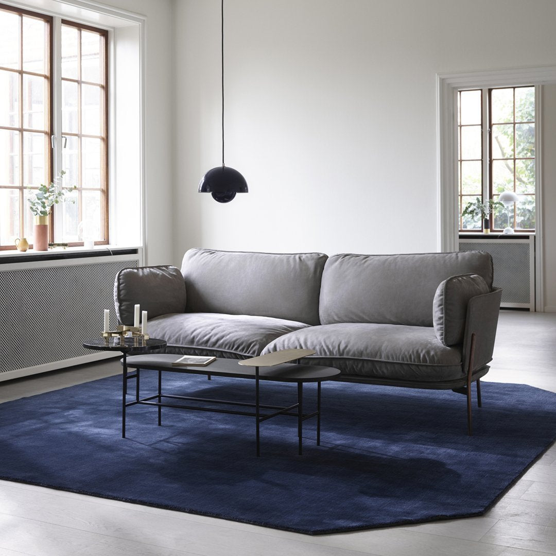 Gray sofa on a dark blue rug in a bright, minimalist room with large windows. Modern and stylish design.