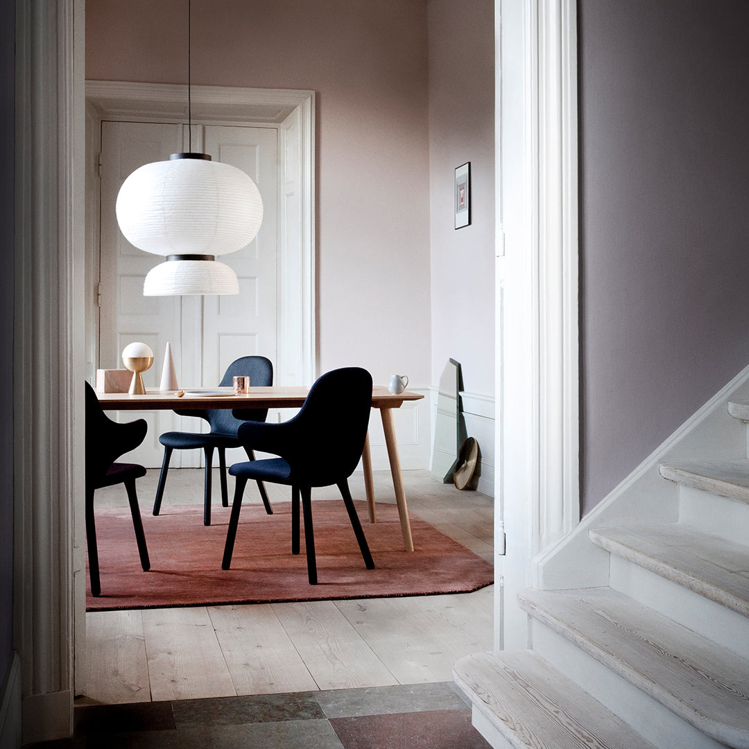 Modern dining room featuring blue chairs, white pendant lights, and a textured, earthy rug in soft pink and brown hues.