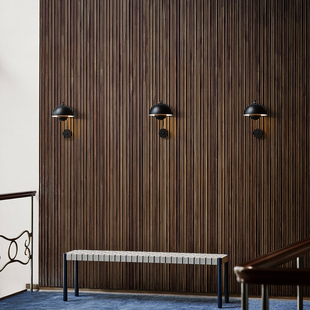 Elegant black wall sconces against a rich wood-paneled backdrop with a blue carpet and a minimalist white bench.