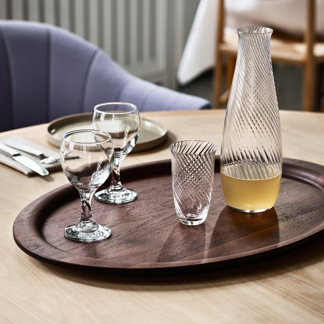 "Clear glassware with diamond patterns on a dark wooden tray against a soft purple background."